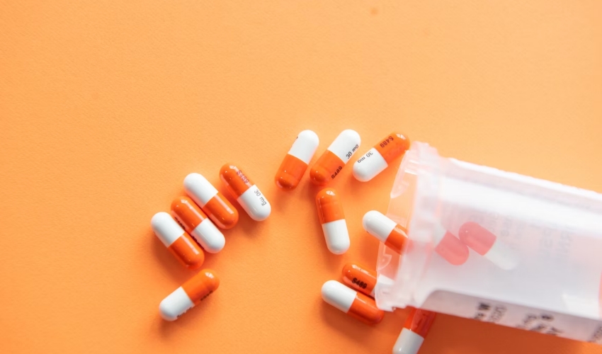 A photo of a bottle of pills spilled out against a solid orange background.
